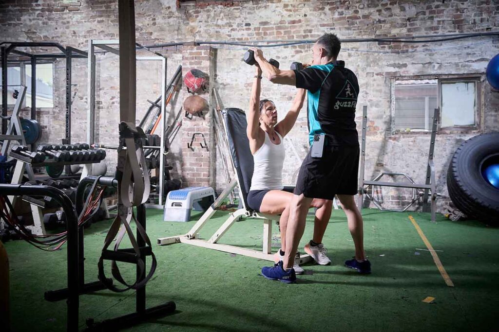 Personal trainer assisting dumbbell shoulder press in Traralgon